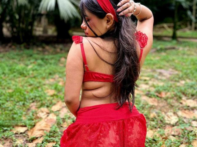 CelesteMorel with long dark hair, red headband, red lace bra, and red sheer skirt, back view, adjusting hair, showing ass and back, standing on grass.
