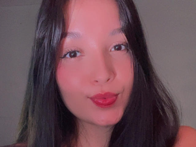 SarahGood has shiny black hair, red lipstick, and a cute smile. Her small tits and pretty face are centered in the image. She looks slightly pouty with pink skin.