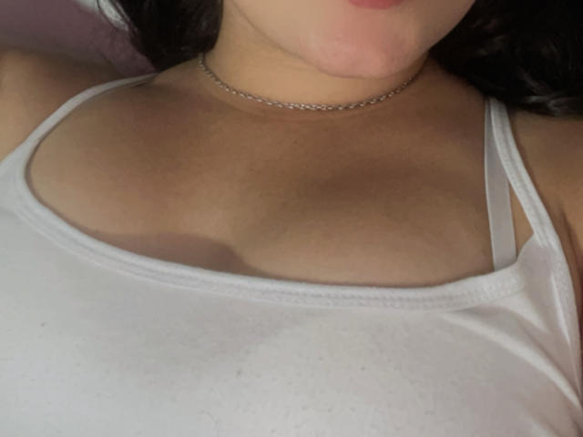 SarahGood's chest with small tits, wearing a white tank top, silver chain necklace, and her lips slightly parted. Her dark hair is partially visible on the right.
