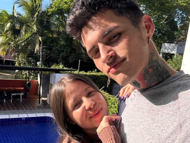 GraceAndTony with short dark hair and tattoos, wearing a gray shirt, next to a smiling woman with brown hair, by a blue-tiled pool. She has blue nails, his neck tattoo.