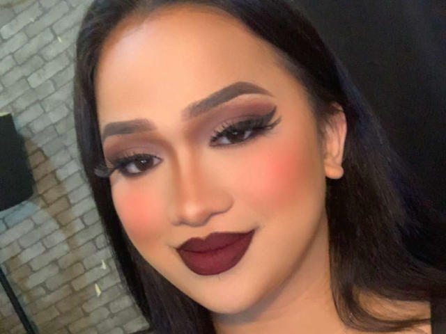 AmaraHugeCock has dark lipstick, thick eyebrows, long eyelashes, and a slightly flushed face. She's smiling with dark hair, and her makeup is bold and attractive.