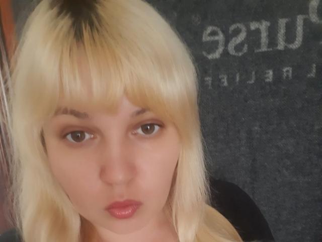 Leylisse has blonde hair with bangs, brown eyes, and pink lipstick. She's looking directly at the camera with a slightly pouty expression. Her ass is not visible.
