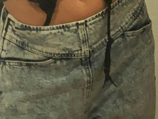 HotCaramelsTrio's ass in tight, distressed, light blue jeans with a black strap from a thong visible above the waistline. The jeans have a noticeable tear on the right.