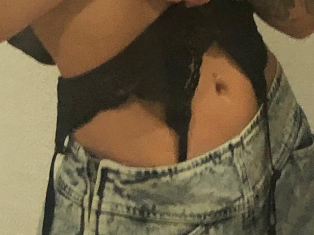 HotCaramelsTrio's midriff showing tan skin, a small belly button, and black lace underwear partially covered by unbuttoned, faded blue jeans.