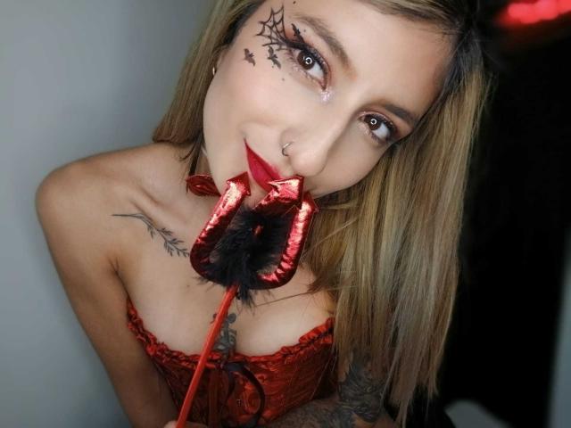 Kaiix, com cabelo loiro, corpete de renda vermelha, piercing no nariz, tatuagens de teia de aranha, segurando um brinquedo sexual de veludo vermelho na boca, tatuagens no pescoço e no braço, sexy, sedutora, tatuada, atraente..