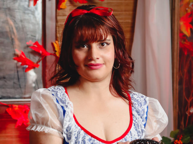 VivianFranco has red hair, a red bow, and wears a blue and white lace dress with puffy sleeves. Her boobs are small, and she's smiling slightly.