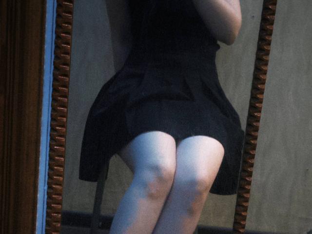 As nádegas e coxas de TiffaniMacandog em um vestido preto, refletidas em um espelho com moldura de madeira, mostrando pele clara e uma leve flexão no joelho..