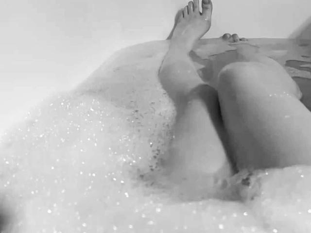 MariannaWarren's legs are in a bubble bath, her feet pointed upwards, with her pussy partially visible through the foamy water. Her hands rest on her knees.