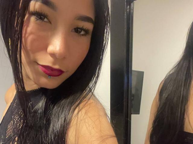 VioletaVelvet with long black hair, dark lipstick, and black mesh top, showing her face and upper chest, reflected in a mirror, with a slightly playful expression.