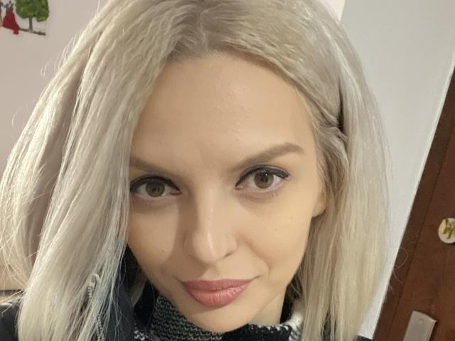 DouceAmelia's face with pale blonde hair, brown eyes, and pink lipstick. She's wearing a black and white patterned scarf. Her ass is not visible. Her tits are small.