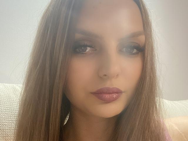 DouceAmelia has straight brown hair, glossy pink lips, and slightly smoky eyes with long lashes. Her skin is fair, and she's looking directly at the camera with a neutral expression.