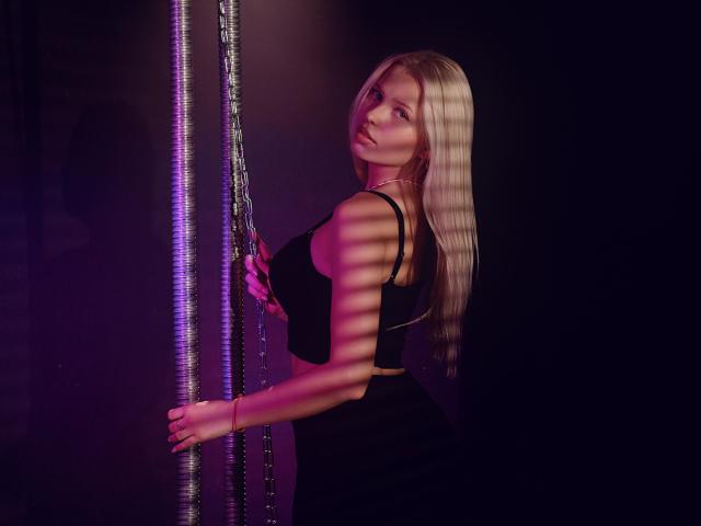 AliceWhitey with long blonde hair, black crop top, and black pants, holding a purple LED strip. Her tits are visible under the top, with a side profile.