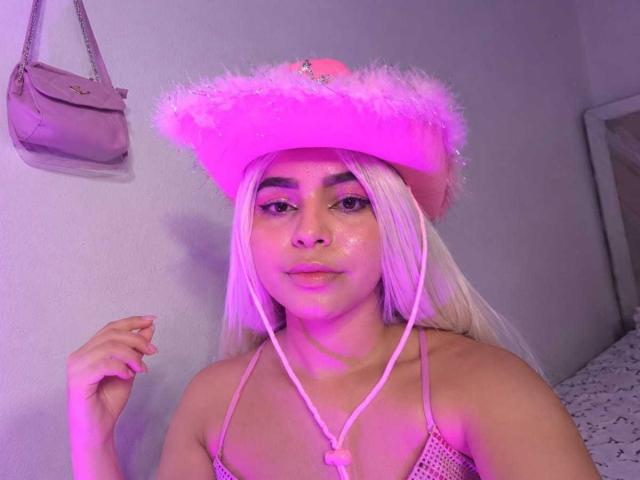 LissyLaurent with pink fluffy hat, white hair, pinkish glow, wearing a tiny mesh top, showing her tits, looking at camera, pink earbuds, hand raised, pink bag on wall.
