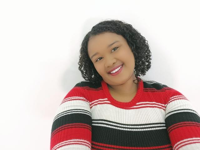 Shehyla, avec ses cheveux noirs bouclés, souriante, portant un pull rayé rouge, blanc et noir, a un visage mignon et attrayant et regarde directement l'appareil photo..