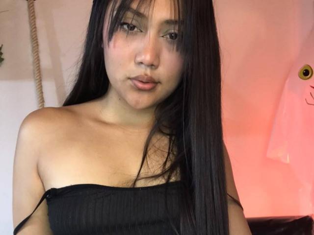Catalehia69 with long black hair, wearing a black strapless top, showing her bare shoulders and small tits, looking at the camera with a neutral expression.
