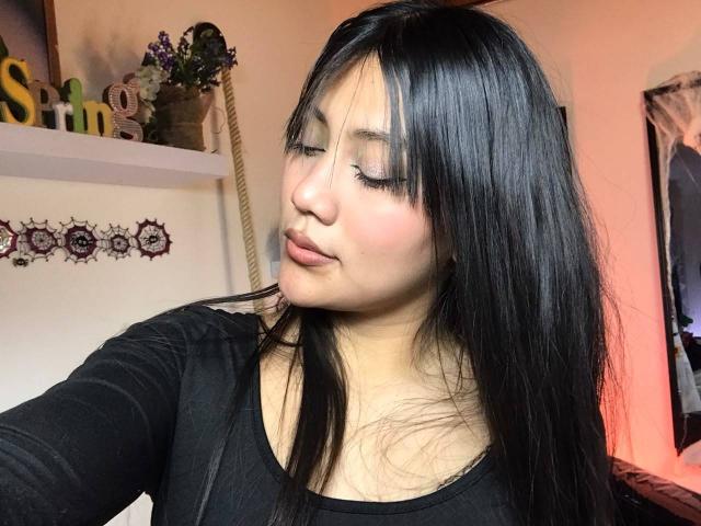 Catalehia69 with long black hair, eyes closed, wearing a black top, soft pink lipstick, and eyeliner, taking a selfie, showing off her pretty face and smooth skin.