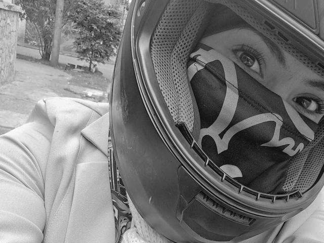 IsaLawrence wearing a helmet with a reflective visor, black mask with white tiger stripes, and a light jacket, showing only their eyes and upper face in a black-and-white photo.