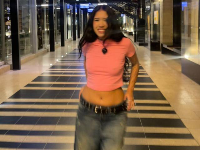 HannaThorne has a pink top, showing her bare midriff, and blue jeans with a black belt. She's smiling, with long black hair, and her ass is slightly visible.
