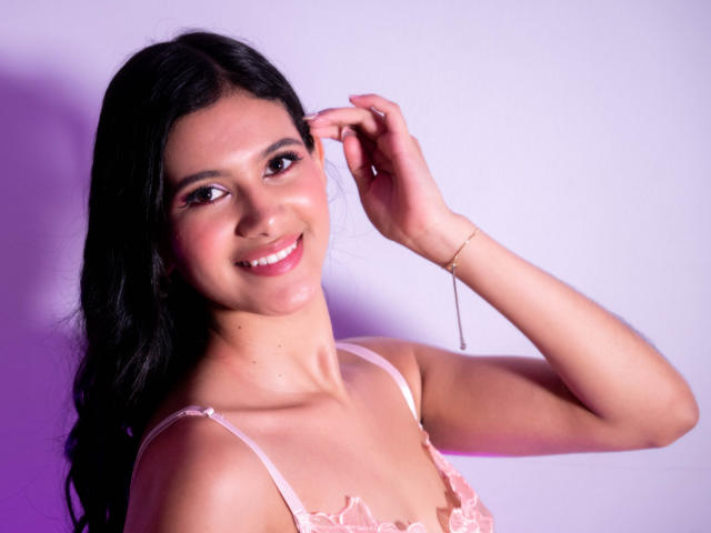 AmilyPreston with black hair, pink lace top, smiling, hand in hair, pink lipstick, bracelet, light skin, cute, boobs, pink eyes, purple lighting, sexy, confident, smiling.