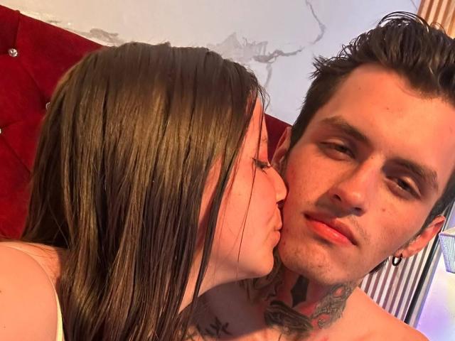 GraceAndTony's brunette chick is kissing Tony's neck, showing off her tattoos. Tony has dark hair, tattoos, and a slightly bored expression. Both are shirtless.