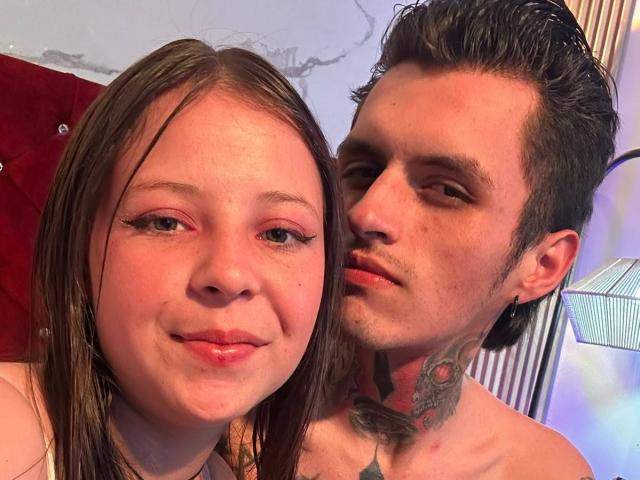 GraceAndTony's face with pink eyeshadow, brown hair, and a slight smile. Tony with dark hair, tattoos, and a mustache, leaning close, smiling. Both shirtless, visible neck tattoos.