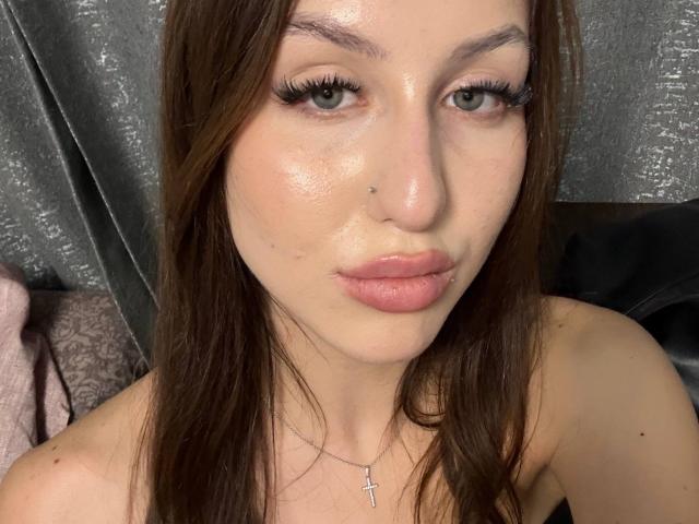 AngelsHazim with shiny skin, brown eyes, long eyelashes, pink lips, brown hair, small nose boogers, cross necklace, looking at camera, slightly pouty face, no clothes visible.