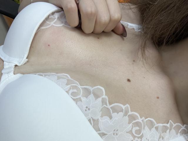 MiraRosse's white bra and lace top, showing her bare skin with small moles and her hand gripping the bra strap, highlighting her tits and soft, light skin.