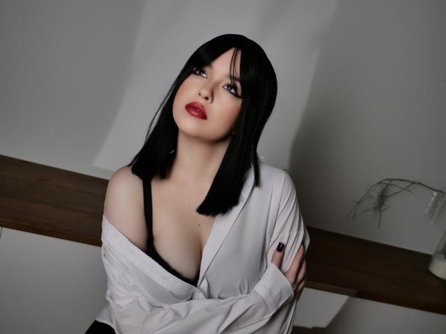 HoneyGlow with black bob, white shirt off shoulders, exposing black bra, red lipstick, looking up, hands crossed, wooden bench, light gray wall, soft lighting, sexy, pale skin.