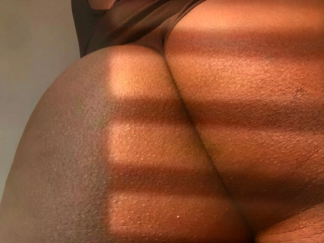 SexyKayla-hot's butt is in the frame, showing her brown, slightly textured skin with sunlight casting striped shadows across her round, prominent ass.