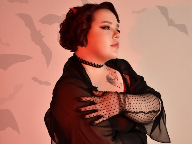 IvoryeFlame with short brown hair, red eyes, black choker, sheer black robe, polka dot gloves, tattoo on chest, crossed arms, looking to the side, red and pink lighting.