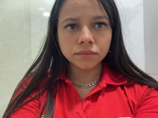 MilaGoddess with long dark hair, red shirt, chain necklace, serious expression, medium skin tone, and small nose, looking at camera. Boobs not visible, ass not visible, pussy not visible.