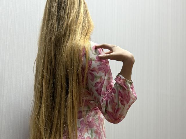 Viloriia's long blonde hair covers her back, wearing a pink floral shirt, right hand touching her hair. Her ass is not visible. Image has a soft, neutral background.