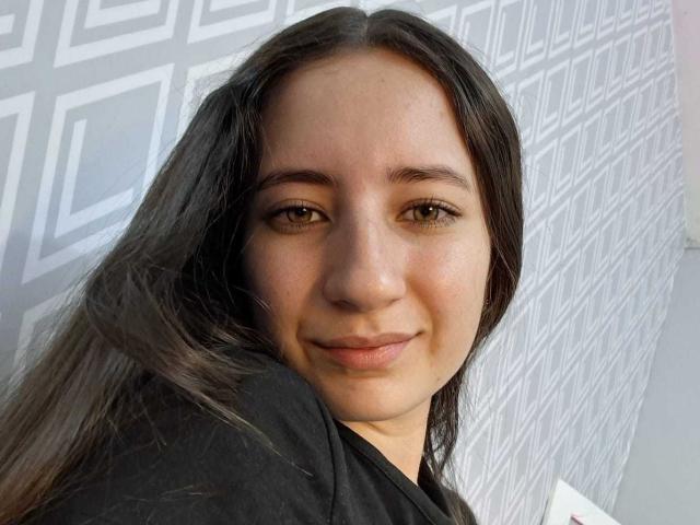 HottieDayCare has long dark brown hair, light brown eyes, and a slight smile. She's wearing a black shirt, and her skin is light with a smooth, natural texture.