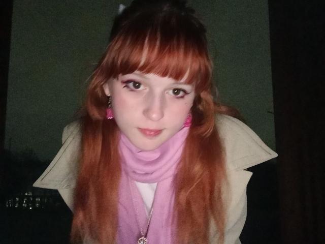 LouieOrner with red hair, pink scarf, white coat, and pink earrings, looking up with a slight smile, wearing a necklace. Her tits are small, and she's cute.