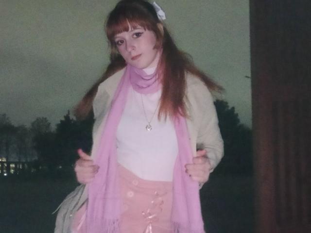 LouieOrner has pale skin, brown hair, and a white hair clip. She's wearing a pink scarf, white top, and pink skirt with button details, looking forward with a slight tilt.