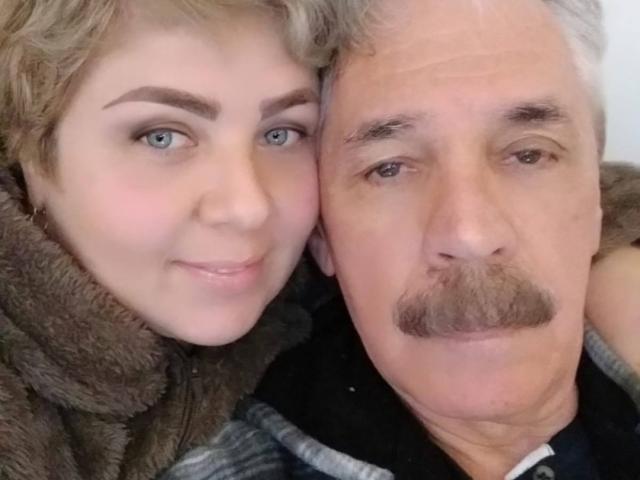 WildLatinCouple ha un viso carino con occhi azzurri e capelli ricci castano chiaro, accanto a un uomo più anziano con i baffi grigi e i capelli bianchi, entrambi sorridenti..