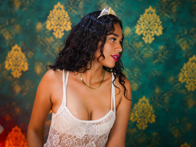ValeryNicolls with curly black hair, wearing a white lace tank top, showing her tits, gold necklace, and cat ears, looking to the side with pink lipstick.