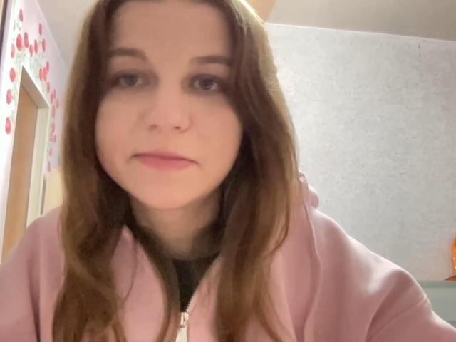 NievesAveles has long brown hair, light skin, and is wearing a pink hoodie with a zipper. Her eyes are half-open, and she's looking directly at the camera.