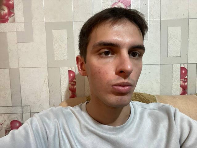 RedEclipse, com uma expressão pensativa, vestindo uma camisa cinza, com cabelo castanho curto e uma leve erupção de acne no nariz, olhando diretamente para a câmera..
