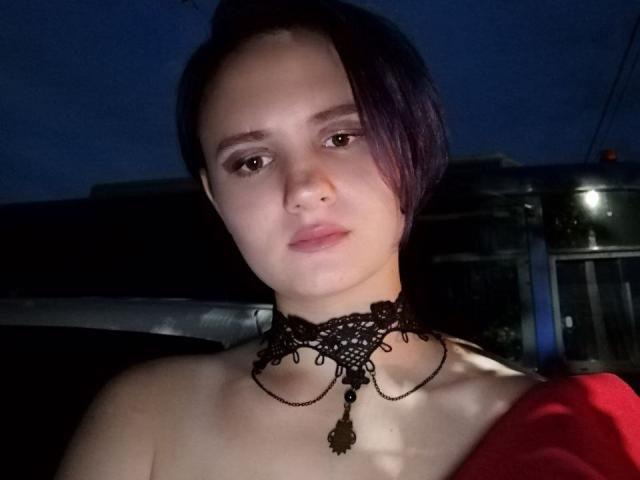 TreenaVisosky with pale skin, dark purple hair, and a black lace choker with a pendant, looking serious, wearing a red garment, night time, dim light.