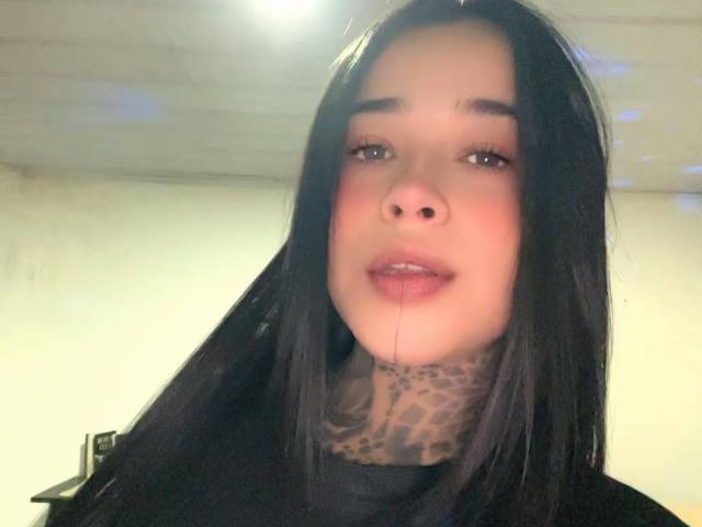 BlackRousse has long black hair, a tattooed leopard-print neck, and a small droplet of saliva hanging from her slightly open mouth. Her face is pale with dark eyebrows.