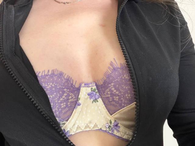 AlicePrings' tits in a purple lace and cream floral bra, visible under a black zip-up jacket. Her skin is light, and she's wearing a silver necklace.