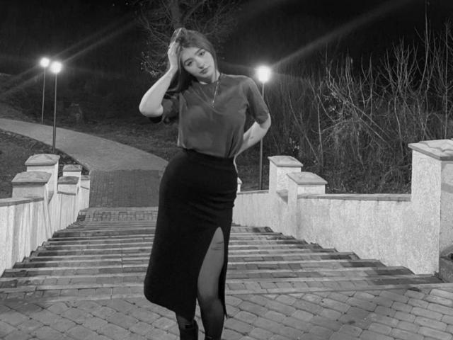 Black-and-white photo of EleanoraMirabal with a hand in her hair, wearing a sheer top and high-slit black skirt, standing on a brick staircase at night. Her tits are visible.