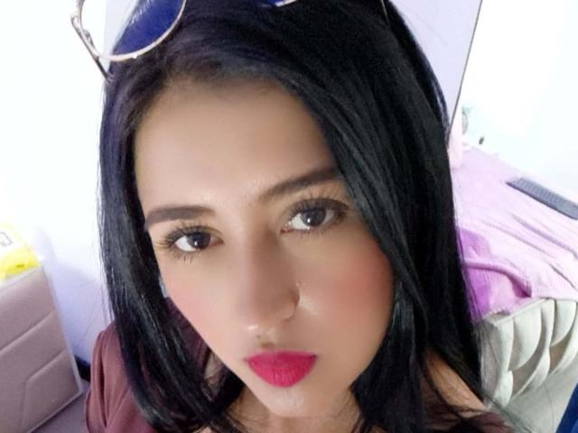 NicollJeans has long black hair, brown eyes, and pink lipstick. She's wearing sunglasses on her head, and has a slightly flushed face, looking directly at the camera.