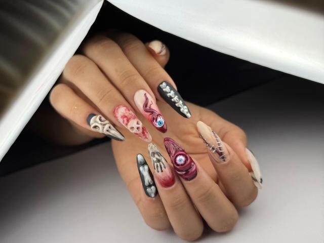 Genesiss' hands with long, elaborate nails featuring creepy, detailed designs: skulls, eyes, snakes, and black patterns on a white background. Boobs are not visible.