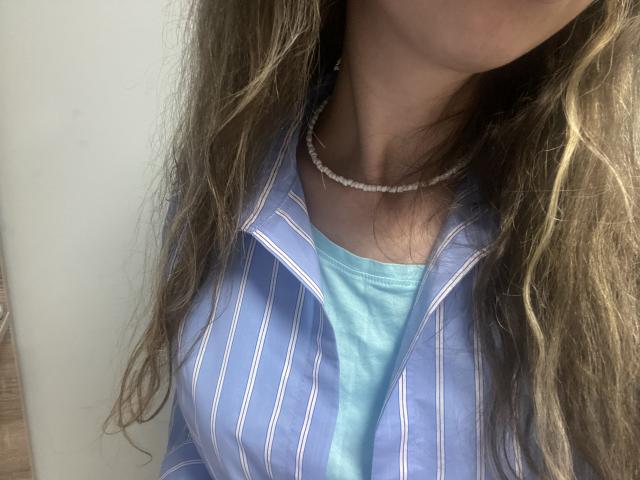 Sanella's chest with a blue striped shirt over a shiny turquoise top, necklace, and long wavy brown hair, partially visible face, sunlight on her skin.