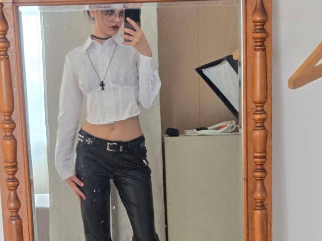LakeshiaPronto in a mirror selfie, wearing a sheer white crop top, black leather pants, and a choker, with a necklace, showing a slim flat stomach and small tits.