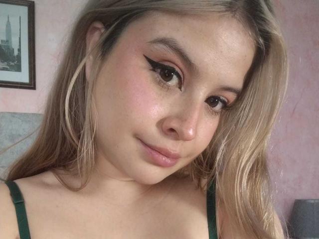 Melani Becker tiene el cabello rubio claro, ojos verdes y un ligero rubor rosado en las mejillas. Lleva tirantes verdes y tiene delineador de ojos alado. Sus labios, ligeramente fruncidos, están ligeramente levantados..