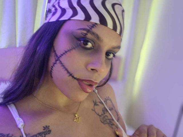TeylorJenkins with purple hair, zebra headband, black eye makeup, and stitches on her face, sucking on a needle, showing tattoos, and wearing a white bra, purple light.
