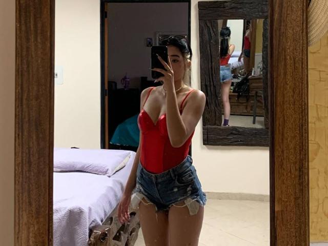StefaValmont in a red, tight, strapless top showing small, perky tits, and short, frayed denim shorts, taking a mirror selfie, with her ass reflected in the mirror.